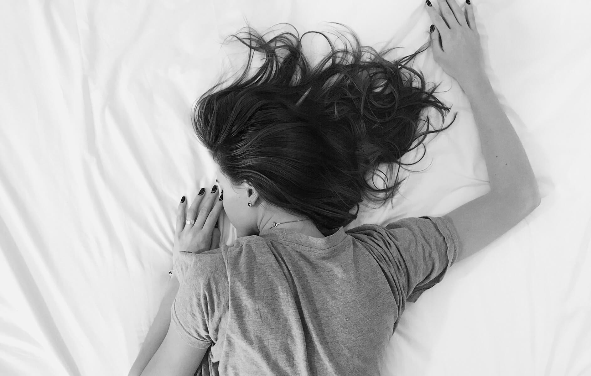 black and white image of a woman laying face down on white bed sheets