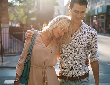 a man and woman walk across a street with their arms around eachother