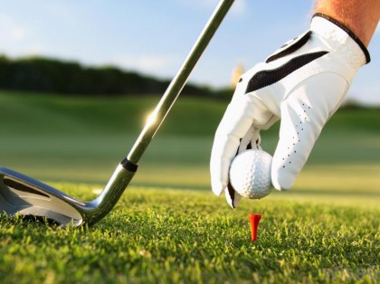 a hand putting a golf ball on a golf tee and holding a golf club