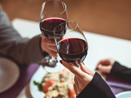 a couple cheersing two glasses of red wine