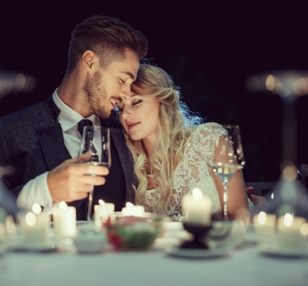 Couple with wine sharing intimate moment at romantic candle lit dinner