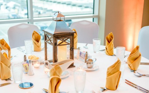 Close up of ballroom table set up for a wedding with a white table cloth, yellow napkins, and a candle holder