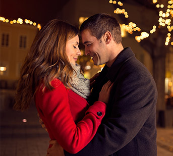 man and woman embracing in with lit up trees behind them