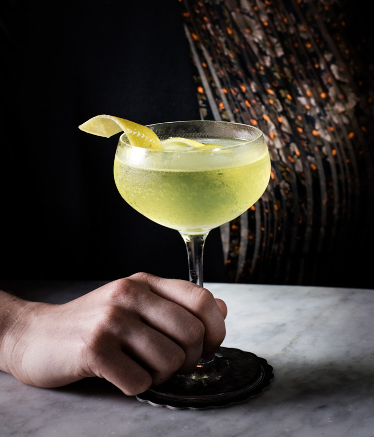 green colored cocktail with a lemon rind garnish