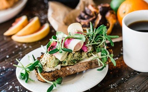a fancy avocado toast sandwich topped with greens and sliced veggies