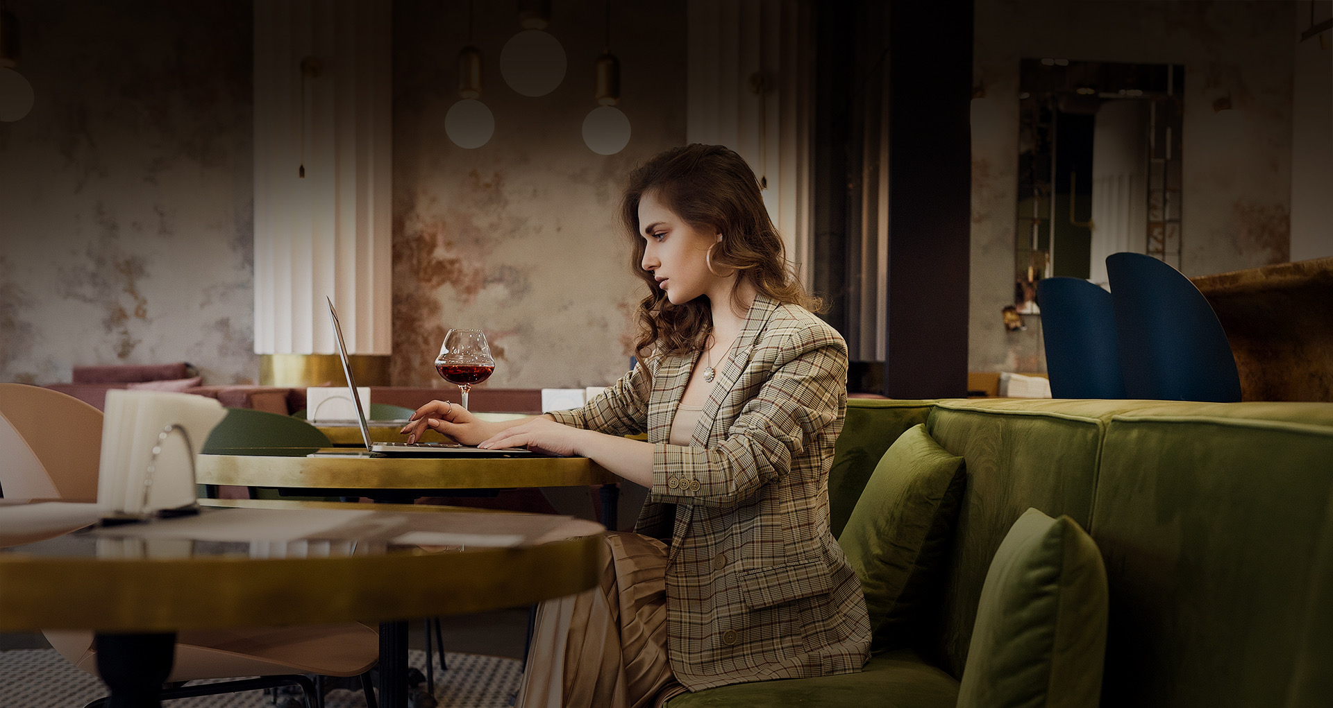 lady in business attire sitting in the dining area, working on her laptop with a side of red wine