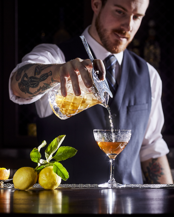 bartender pouring an orange cocktail into a glass