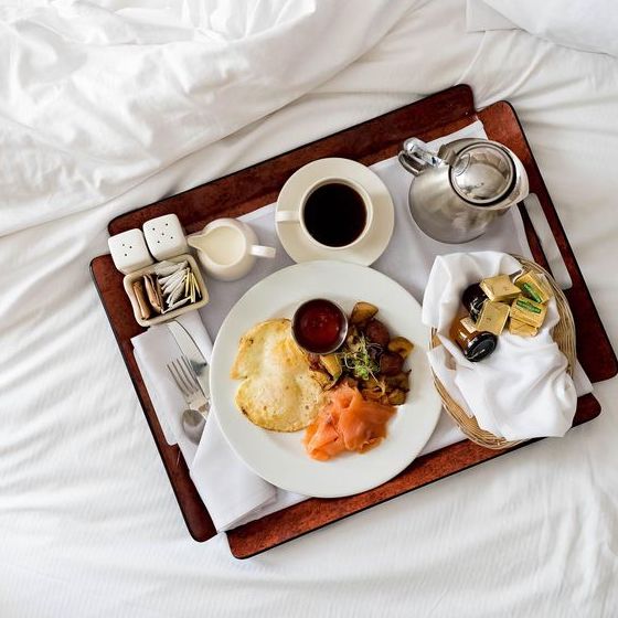 dark wood tray filled with breakfast items placed on top of white bedsheets
