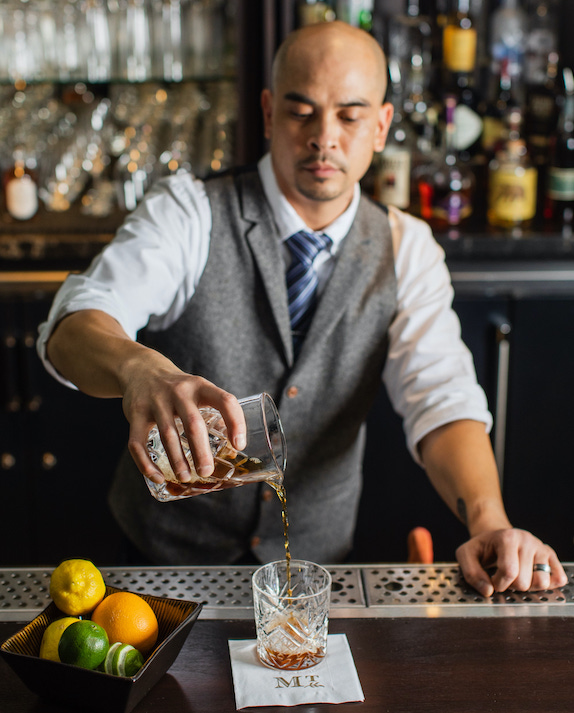 bartender pouring dark liquor into glass