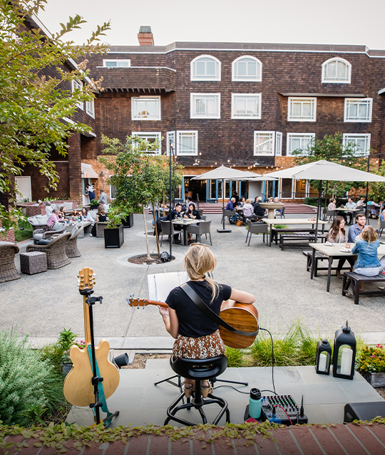 customers sitting at tables outside Menlo Tavern while listening to woman play guitar on stage
