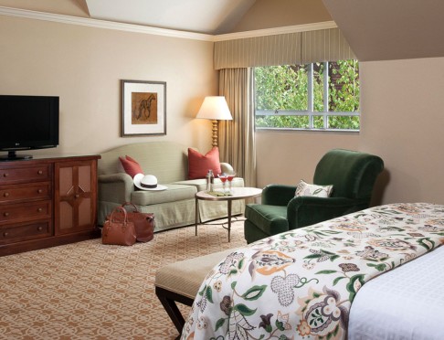 Queen bed with floral duvet, sitting area with loveseat and chair and tv on dresser