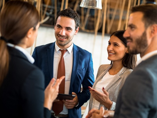 a group of business people talking to each other and smiling