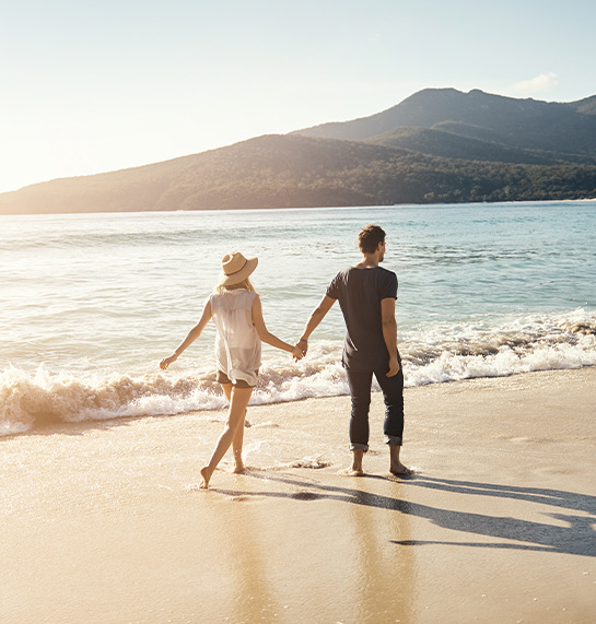A man and woman walking down the beach at sunset.