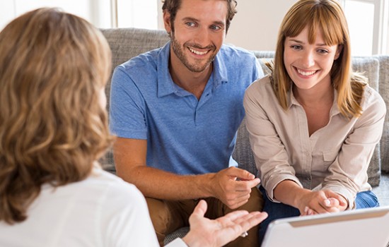 A smiling man and woman talking to a lady with a tablet.