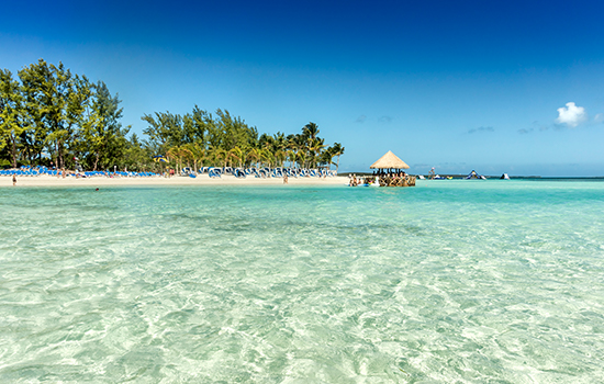 A tiki hut next to the clear blue water.