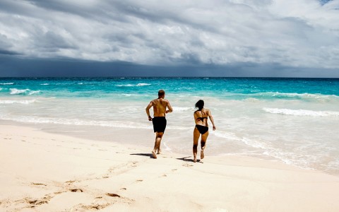 a man and a woman running towards the water at the beach