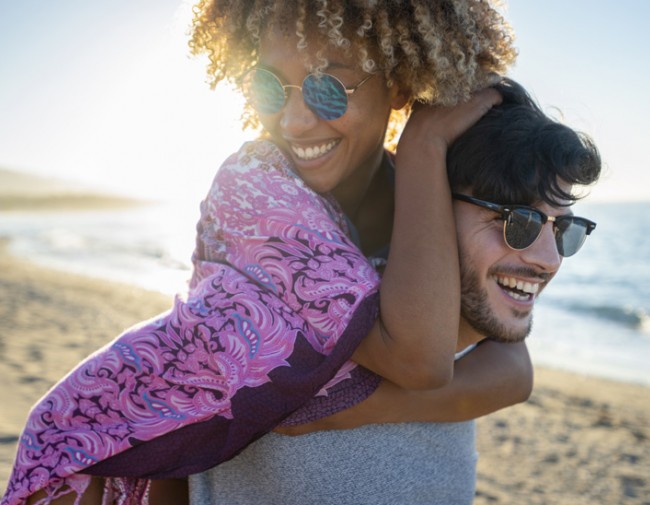 girl on the piggy-backing on a guy as he walks down the beach
