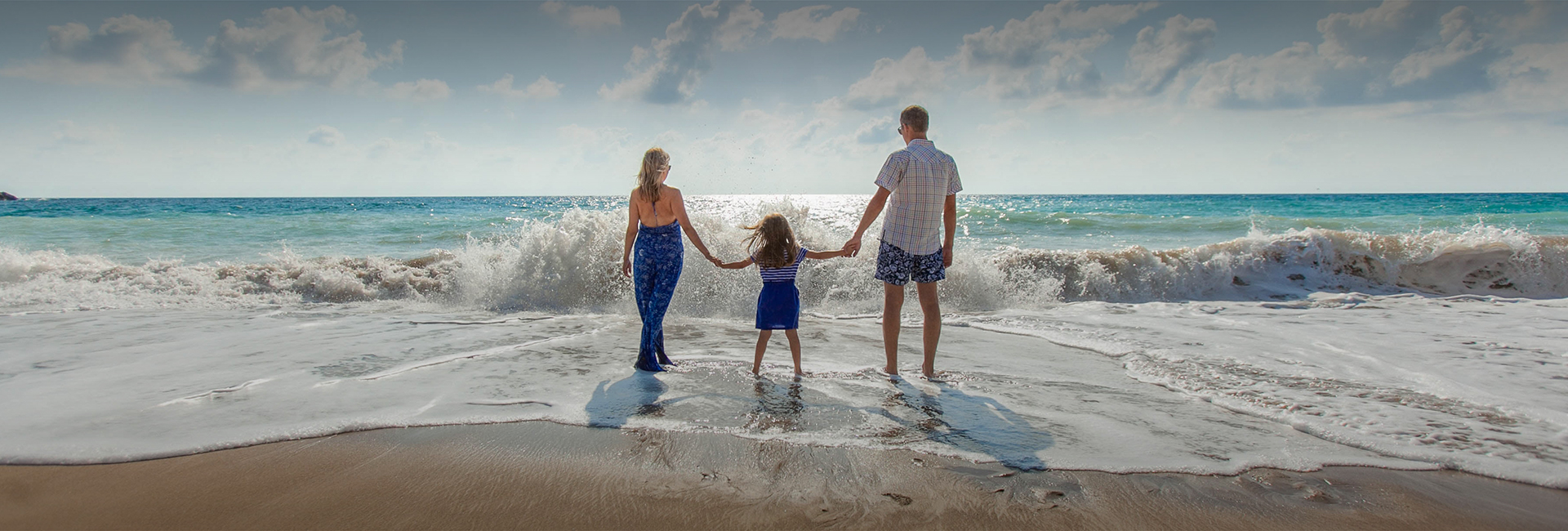 mom and dad holding their daughters hand at the edge of the water on the beach