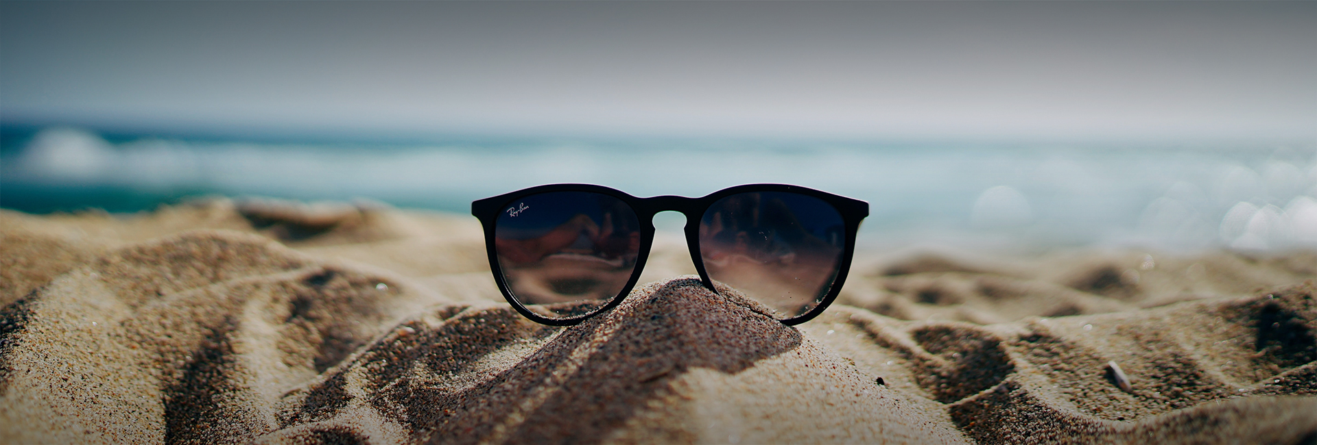 sunglasses in the sand with the ocean in the background