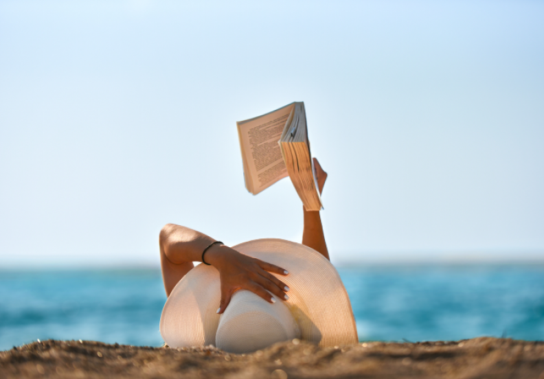 women laying on beach reading a book