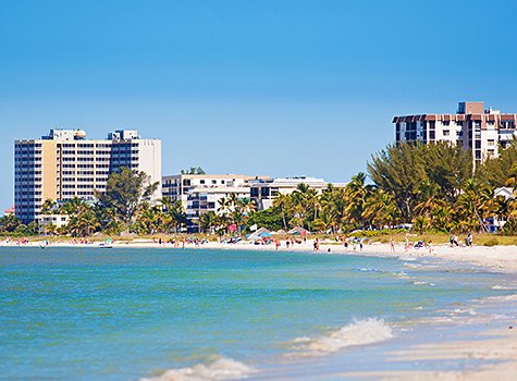 white sand beach and blue water with high-rises in background