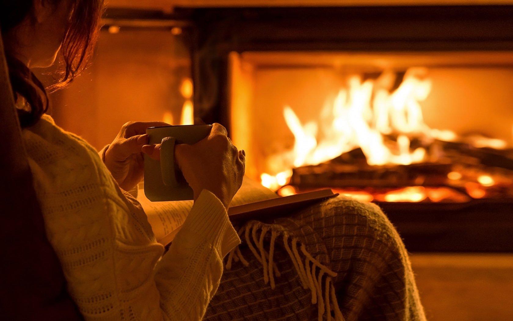 woman snuggled up drinking coffee by the fireplace
