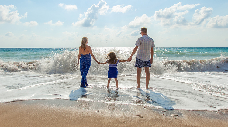 family of three holding hands walking into the ocean