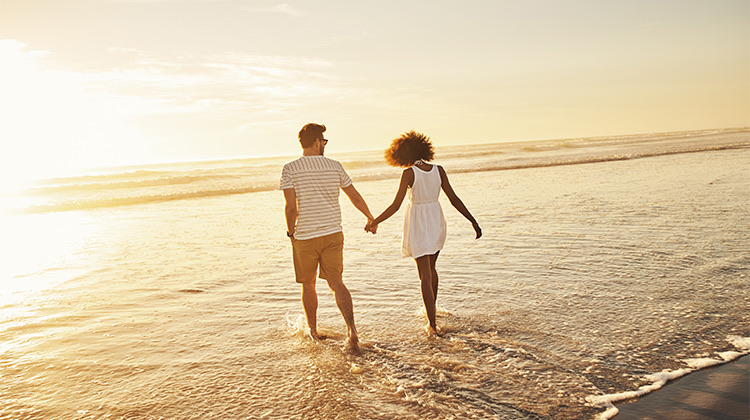 a couple holding hands and walking into the ocean