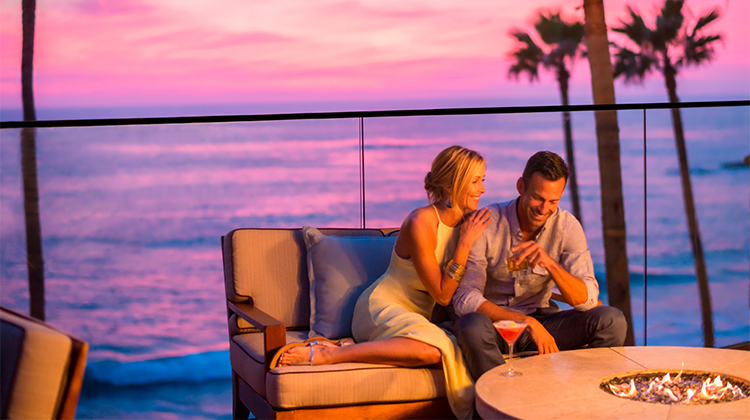 man and woman laughing in front of a fire-pit during sunset