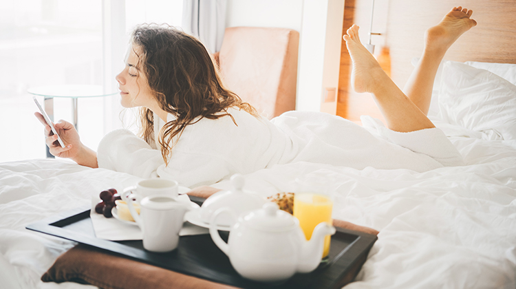 woman on her phone laying on her stomach next to her breakfast in bed