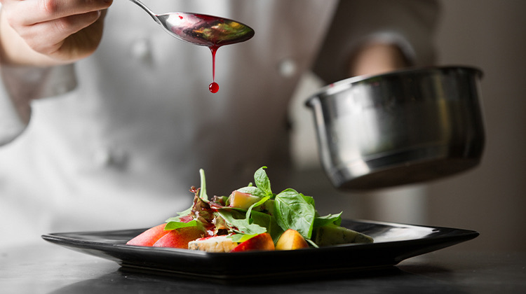 close up of a chef pouring a red sauce on a dish