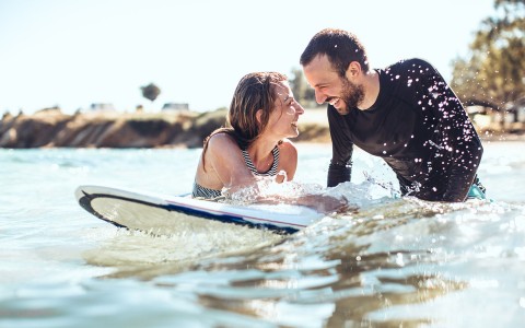 man and woman in the ocean on a surfboard laughing