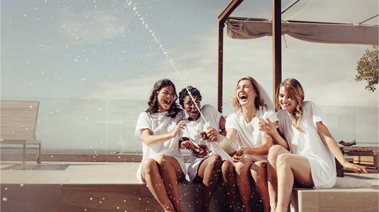 group of women laughing and popping a bottle of champagne