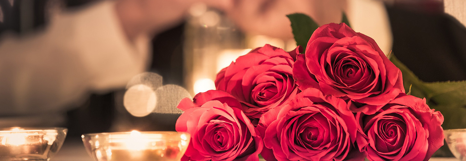 roses and candles on a table with a couple holding hands in the background