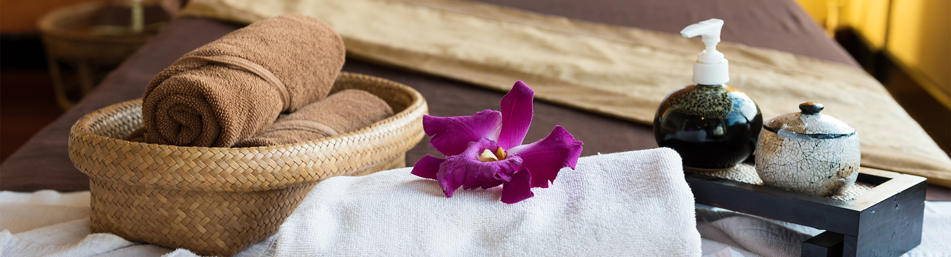 basket of brown towels next to a white towel with a purple flower on top