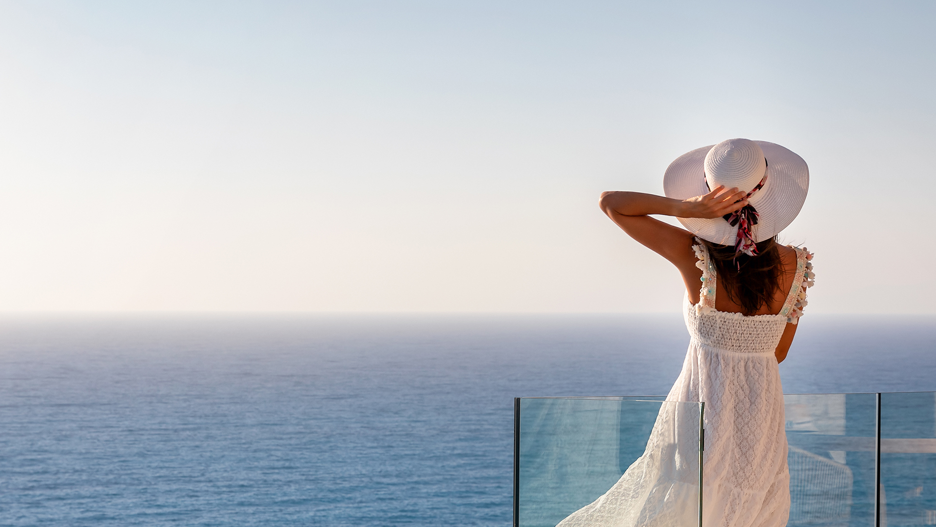 woman with a white dress holding her hat while looking at the ocean
