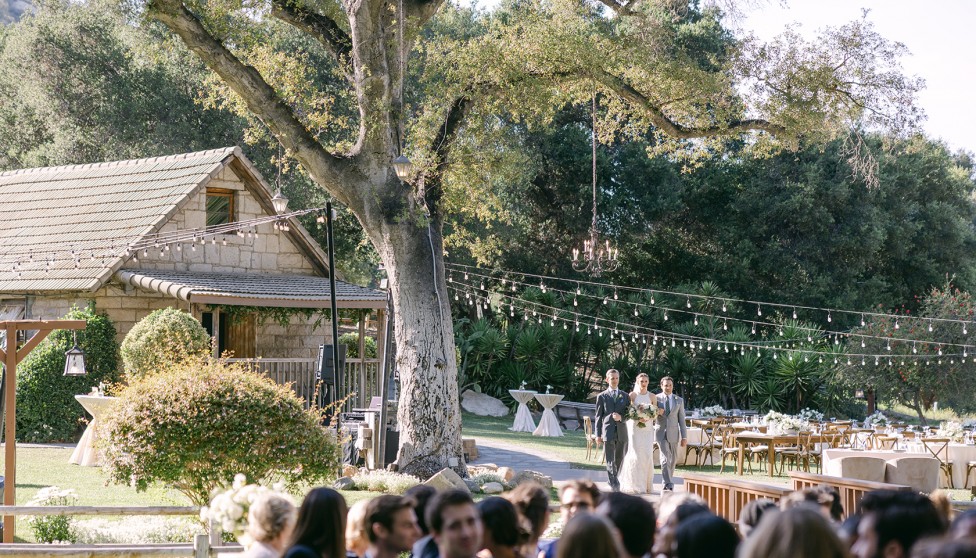 wooden bridge over grass leading to an outdoor wedding reception
