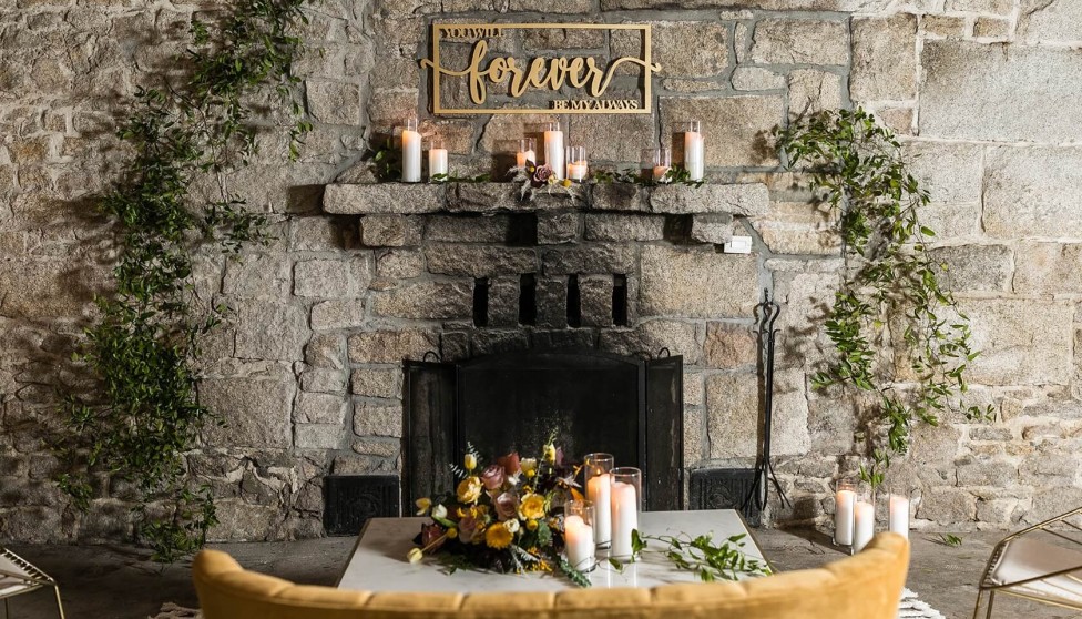 stone fireplace decorated with greenery, candles, and a sign