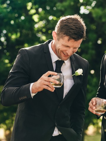 two men in suits holding drinks and laughing