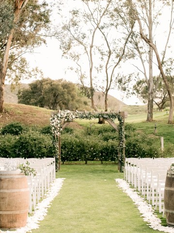 outdoor wedding ceremony with a wooden centerpiece, wooden barrels, and white chairs