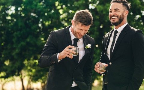 two men in tuxedos laughing over a drink