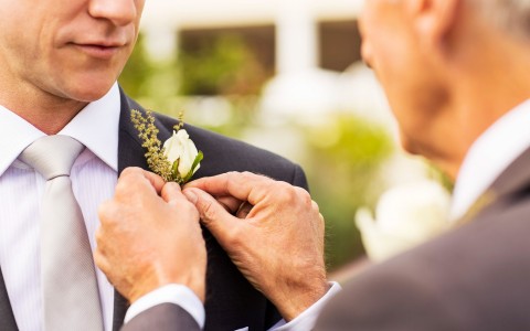 closeup view of a guy putting a small rose close to the shoulder of the groom