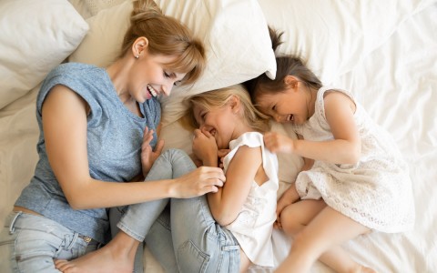 a mom and her girls laying on a bed and laughing 