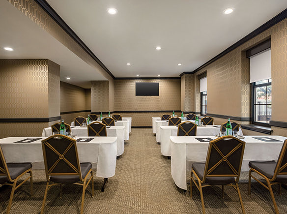 meeting space with white table clothes, 8 tables, and gold and black chairs