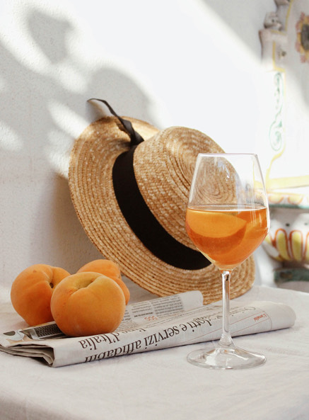 
                            orange cocktail sitting on a white surface next to a sun hat, oranges, and the newspaper