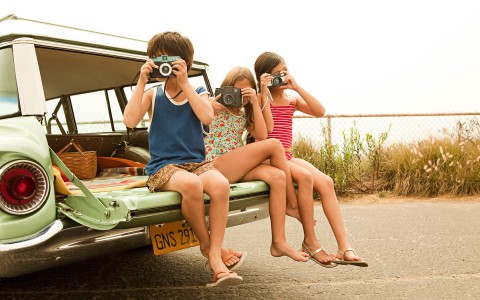 little kids holding camera while sitting on the back of a truck 