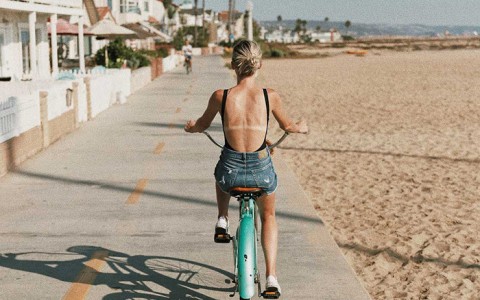 woman riding a bike near the beach with buildings on the left 