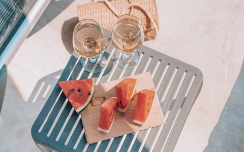 aerial image of watermelon cut into triangles and tow wine glasses on an outdoor table