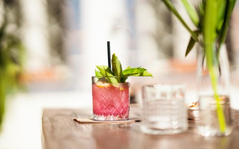 pink cocktail garnished with leaves and a straw sitting on a coaster