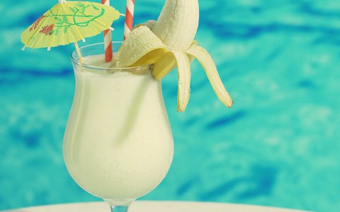 pina colada by the pool topped with a banana two straws and a little umbrella